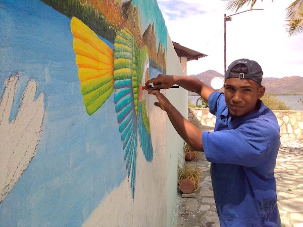 A man paints a mural with birds on it
