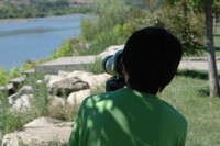 Boy bird watches by the river with binoculars
