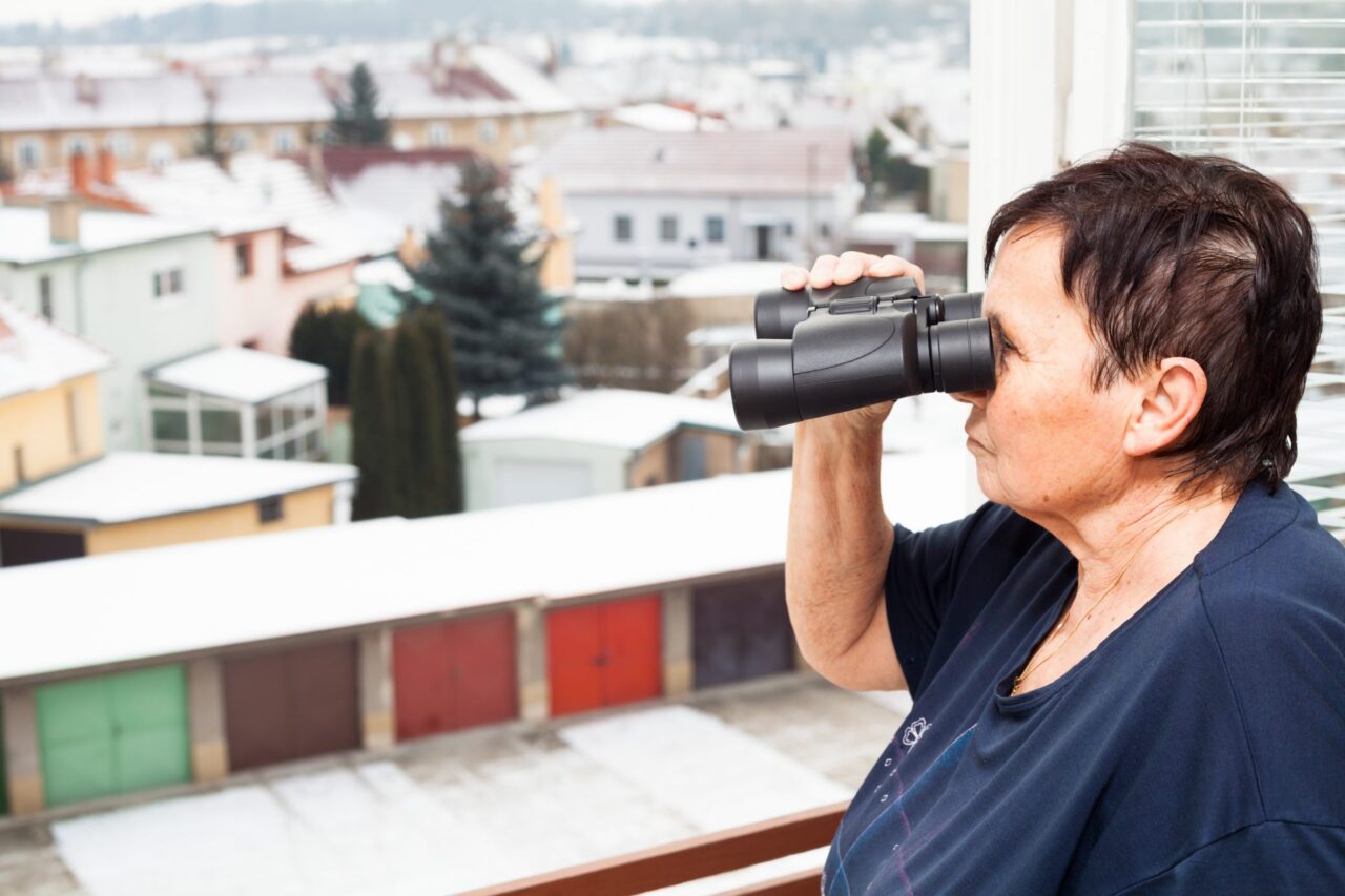 Woman looking out a window through binoculars